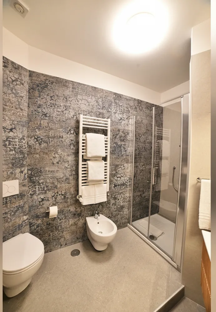 Il bagno con le piastrelle in pietra scura, il box doccia in cristallo, i sanitari sospesi e lo scaldasalviette